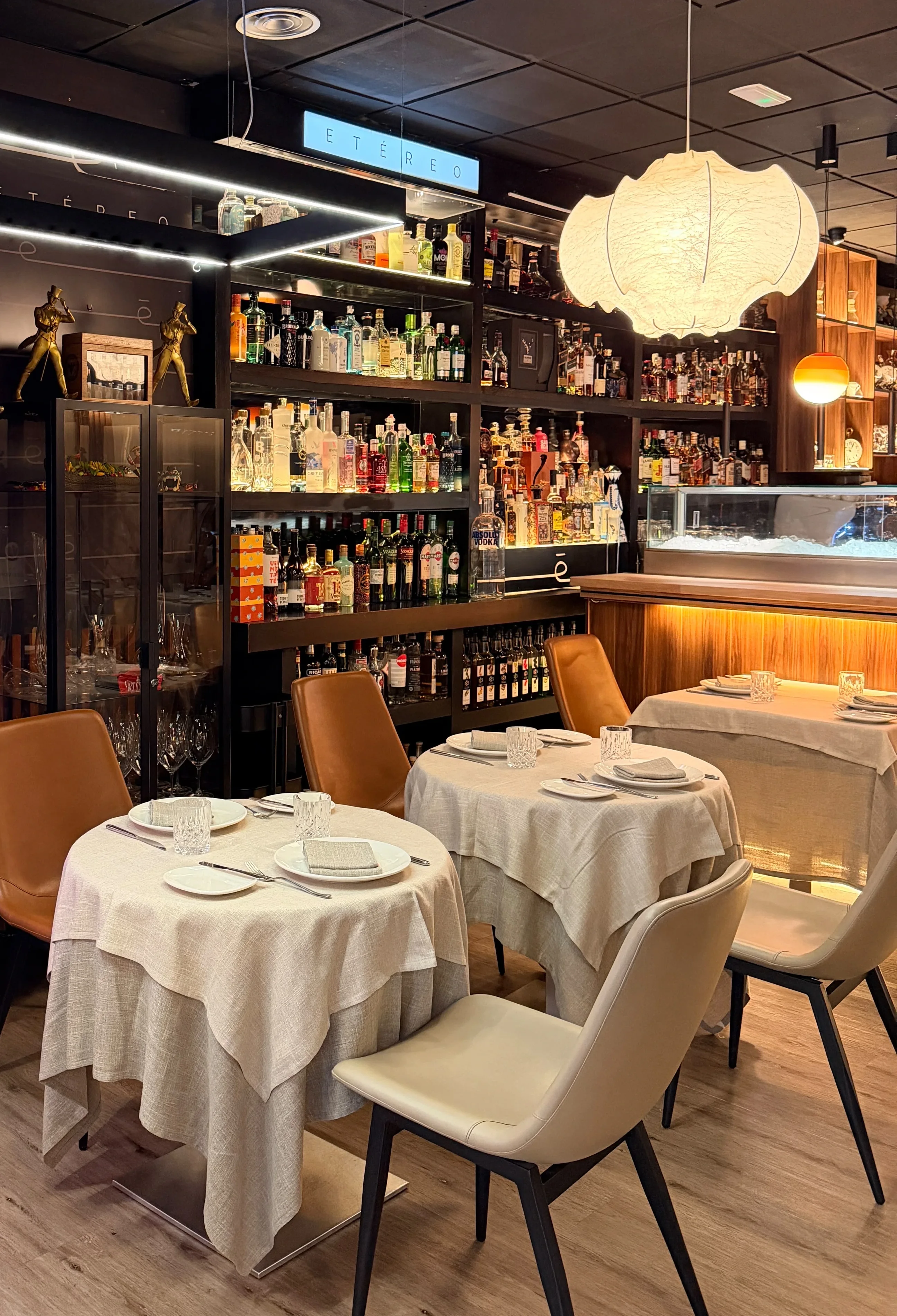 La sala de Etéreo: mesas con mantel de lino, sillas de piel, el botellero iluminado y una lámpara de papel
